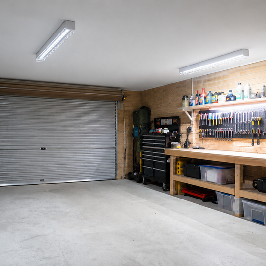 Garage with wire guard batten lights and tools and equipment on shelves and a workbench.